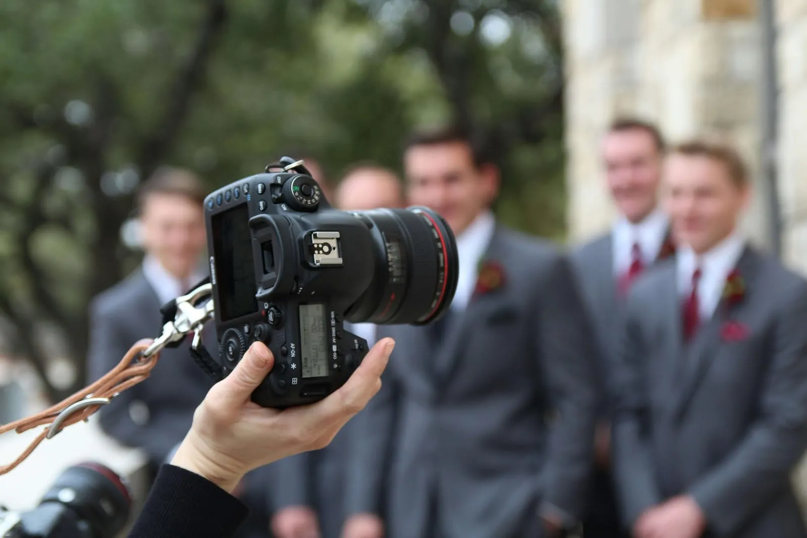 Fotograf s fotoaparátom v ruke fotí ženícha a svedkov pred kostolom